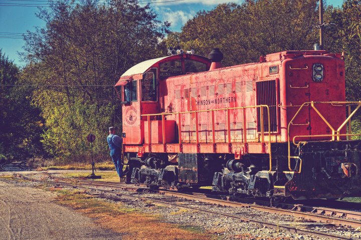 A train with a man hanging off the side for a ride.