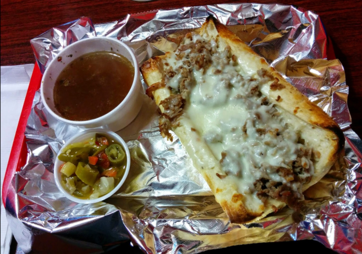 A french dip sandwich covere din cheese next to au jus.