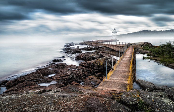 The Grand Marais lighthouse on a foggy Summer morning located on the Grand Marais Harbor - Artists Point, Minnesota, USA. Big Marsh is the direct translation of the French Grand Marais. While the name was given by Voyageurs in the early seventeenth century, many subsequent observers were puzzled, since no marshes have ever been known to exist here. However, it is believed that the Voyageurs had their own unique vocabulary, and it is likely that Marais referred to a cove, or harbor of refuge.