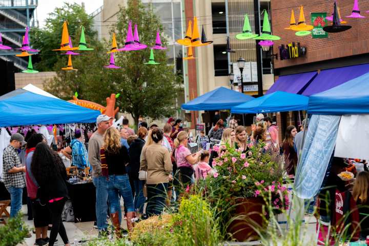 A crowded fall festival with multi-colored witch hats overhead.