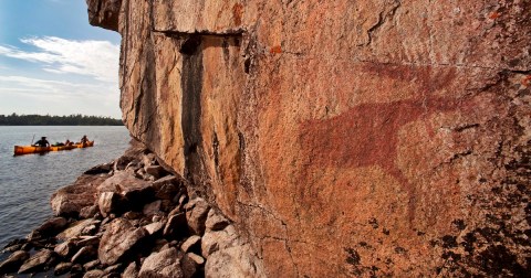 Canoeists paddle by pictographs on Lac La Croix Lake. The pictographs date back several hundred years, and are painted on cliffs on Minnesota's Lac La Croix Lake in the Boundary Waters Canoe Area Wilderness.