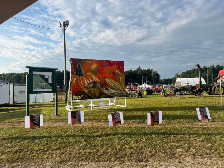 A fairground with a giant painting of autumnal vegetables, and farm equipment in the background.