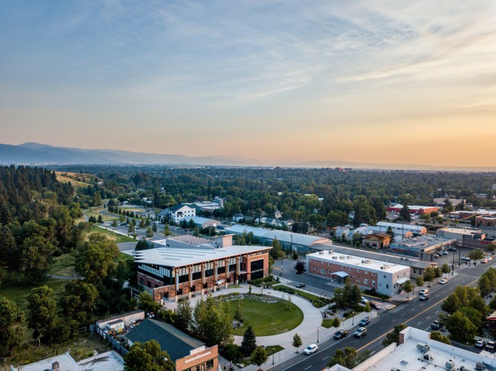 Aerial view of Main Street in downtown Bozeman Montana at sunset. The suns rays are hitting the rooftops and casting golden shadows. The street is lined with businesses on a summer day.