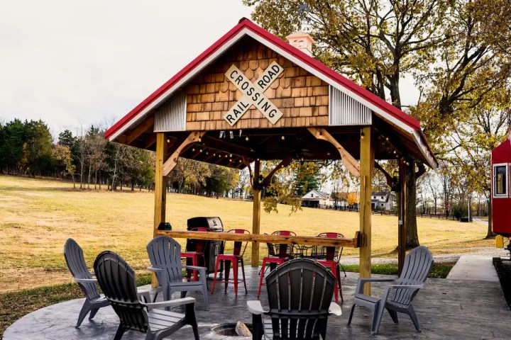 Grey chairs around a fire pit area and a red-roofed pavilion behind it.